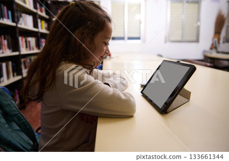 Young Girl Studying At Library Table With Tablet, Focused Learning Moment 133661344
