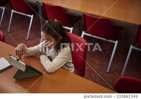 Young Girl Using Tablet at Classroom Desk in a School Library Setting 133661349