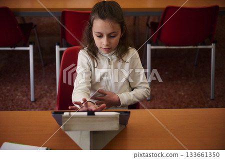 Young Girl Studying on Tablet in School Library During Classroom Session Young Girl Studying on Tablet in School Library During Classroom Session 133661350