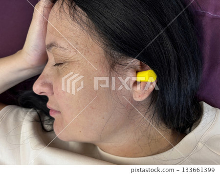 Close up of adult brunette woman sleeping with yellow earplugs, noise protection for healthy sleep, deep rest, insomnia prevention and peaceful home bedroom atmosphere Close up of adult brunette woman sleeping with yellow earplugs, noise protection for healthy sleep, deep rest, insomnia prevention and peaceful home bedroom atmosphere 133661399