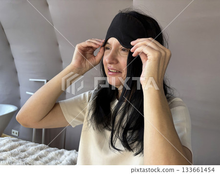 Adult brunette woman sitting in bed with a sleep mask, smiling and looking relaxed after a good night sleep, cozy morning routine, healthy sleep, wellness and self care lifestyle Adult brunette woman sitting in bed with a sleep mask, smiling and looking relaxed after a good night sleep, cozy morning routine, healthy sleep, wellness and self care lifestyle 133661454