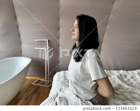 Adult woman stretching and massaging her back after waking up, morning muscle relaxation, recovery after sleep, healthy daily routine and wellness lifestyle 133661629