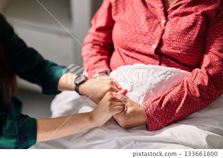 Holding hands in a caring moment between generations in a hospital room during the afternoon Holding hands in a caring moment between generations in a hospital room during the afternoon 133661800