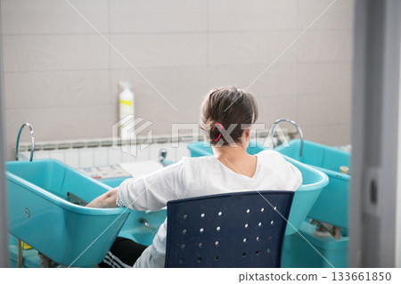 Patient undergoing hydrotherapy treatment with arms immersed in blue rehabilitation tubs inside wellness facility Patient undergoing hydrotherapy treatment with arms immersed in blue rehabilitation tubs inside wellness facility 133661850
