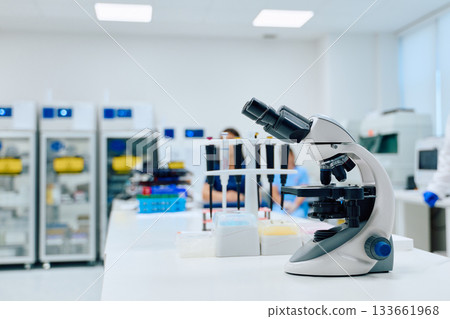 Microscope in a modern laboratory with scientists conducting research during daylight hours 133661968