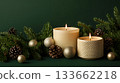 Two candles are lit on a green background with pine cones and gold ornaments 133662218