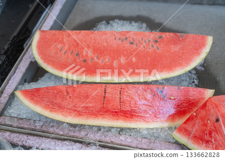 Bright red watermelon slices displayed on a chilled surface. The juicy flesh and fresh texture highlight summer refreshment and natural sweetness, ideal for food, nutrition or seasonal lifestyle Bright red watermelon slices displayed on a chilled surface. The juicy flesh and fresh texture highlight summer refreshment and natural sweetness, ideal for food, nutrition or seasonal lifestyle 133662828