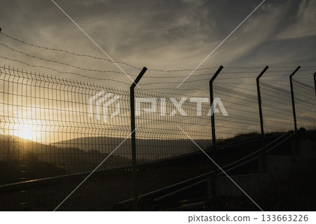 Border Fence at Sunset. Migration and Political Tension Concept 133663226