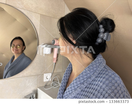 Adult woman in bathrobe standing in front of bathroom mirror applying skincare patches, home beauty routine, rejuvenating facial treatment, wellness and self care concept Adult woman in bathrobe standing in front of bathroom mirror applying skincare patches, home beauty routine, rejuvenating facial treatment, wellness and self care concept 133663373