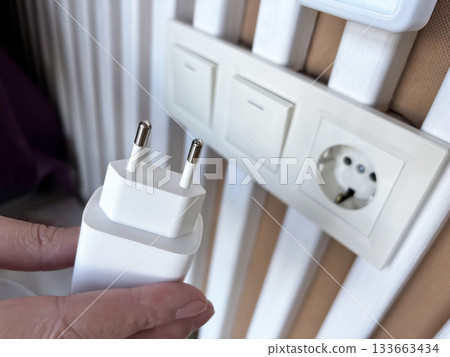 Hand plugging a phone charger into a wall socket, connecting power adapter at home, charging mobile device, everyday technology use and modern lifestyle concept 133663434