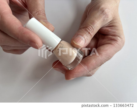 Woman holding a beige nail polish bottle while preparing to paint her nails at home. Close-up of female hands during nail care routine. Natural manicure concept, beauty and self-care at home 133663472