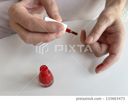 Woman accidentally smudging nail polish and getting her fingers messy during a home manicure. Close-up of hands with spilled polish. Imperfect nail painting, beauty routine at home	 133663473