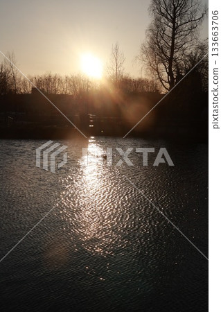 The sun is setting over a body of water, casting a warm glow on the surface The sun is setting over a body of water, casting a warm glow on the surface 133663706