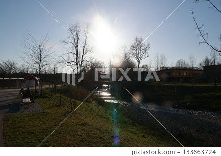 A man sits on a bench in a park, watching the sun set 133663724