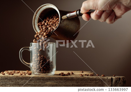Roasted coffee beans is poured in a clear glass mug. 133663997