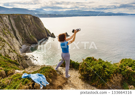 Tourist with camera on Asturias coast. Cabo Busto cliffs, Spain. Tourist with camera on Asturias coast. Cabo Busto cliffs, Spain. 133664316