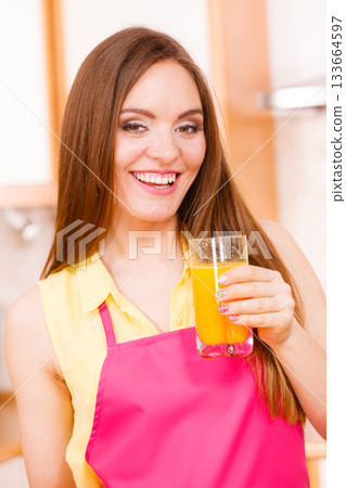 Woman in kitchen drinking fresh orange juice 133664597