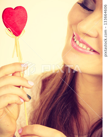 Flirty woman holding red wooden heart on stick Flirty woman holding red wooden heart on stick 133664606