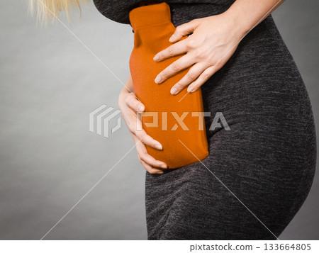 Girl having stomach ache, holding hot water bottle Girl having stomach ache, holding hot water bottle 133664805