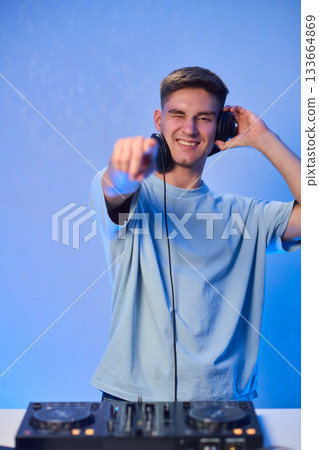 Young DJ with headphones, Skilled DJ engaging with equipment in lively environment, Energetic DJ prepping for live performance amid colorful lighting and fashionable attire Young DJ with headphones, Skilled DJ engaging with equipment in lively environment, Energetic DJ prepping for live performance amid colorful lighting and fashionable attire 133664869
