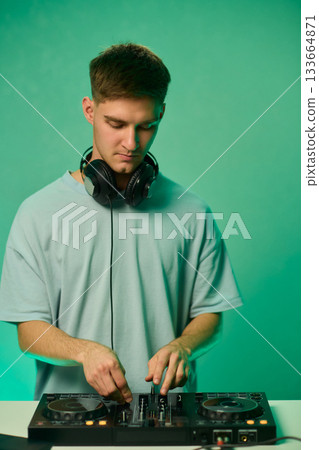Young DJ with headphones, Skilled DJ engaging with equipment in lively environment, Energetic DJ prepping for live performance amid colorful lighting and fashionable attire Young DJ with headphones, Skilled DJ engaging with equipment in lively environment, Energetic DJ prepping for live performance amid colorful lighting and fashionable attire 133664871