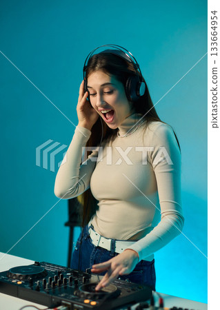 Female DJ mixing on turntables, colorful lighting studio, focused expression, hands adjusting mixer and laptop controls, wearing headphones, modern electronic music vibe, cinematic lighting 133664954