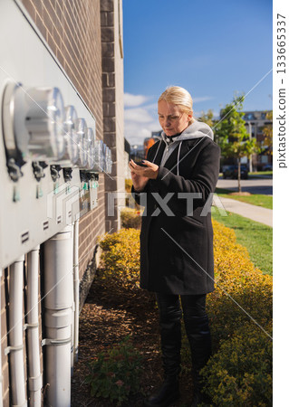 Woman checking outdoor electricity meters on building wall using smartphone 133665337