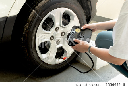 Woman using portable tire inflator with pressure gauge to check and inflate car wheel. Auto maintenance safety concept. 133665346