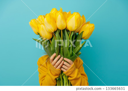 A joyful child peeks out from behind a colorful bunch of yellow tulips, wearing a cozy yellow sweater in a cheerful blue backdrop, capturing a moment of innocence A joyful child peeks out from behind a colorful bunch of yellow tulips, wearing a cozy yellow sweater in a cheerful blue backdrop, capturing a moment of innocence 133665631
