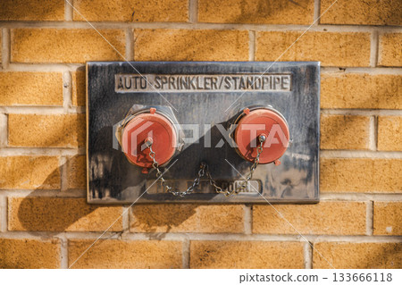 Fire department connection with dual standpipe and auto-sprinkler caps mounted on a brick wall in bright sunlight Fire department connection with dual standpipe and auto-sprinkler caps mounted on a brick wall in bright sunlight 133666118