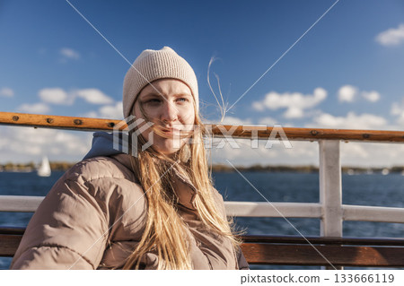 Young woman in a warm jacket and knit hat sitting on a boat on a sunny windy day over Lake Ontario in Toronto, Canada 133666119