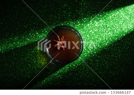 Christmas Holiday Spiced Hot Drink. Glass Cup with Mulled Wine and Star Anise on Glittery Green Background Christmas Holiday Spiced Hot Drink. Glass Cup with Mulled Wine and Star Anise on Glittery Green Background 133666187