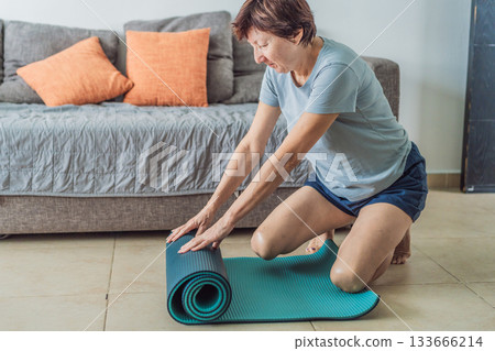 Elderly woman practicing yoga in her cozy living room, stretching on a mat and maintaining balance. Concept of healthy aging, active senior lifestyle, mindfulness, wellness, and daily home exercise 133666214