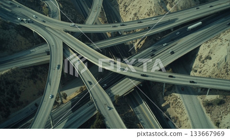 Cars and trucks are driving on a complex highway interchange crossing a barren landscape, creating a network of interconnected roads and bridges 133667969