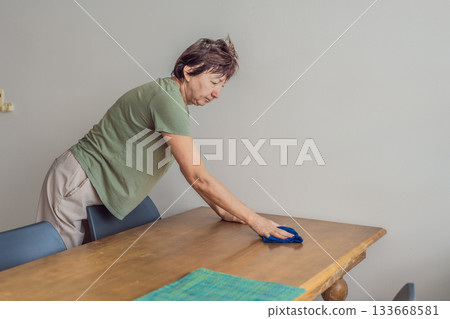 Unaltered senior woman cleaning and organizing a table at home, creating a tidy and comfortable living space. Concept of everyday routine, home care, cleanliness, wellbeing, responsibility and simple Unaltered senior woman cleaning and organizing a table at home, creating a tidy and comfortable living space. Concept of everyday routine, home care, cleanliness, wellbeing, responsibility and simple 133668581