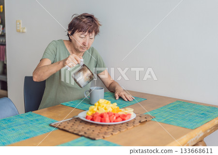 Unaltered senior woman enjoying a calm breakfast at the dining table in a bright home setting. Concept of healthy lifestyle, mindful eating, peaceful morning routine, comfort, wellbeing and everyday 133668611