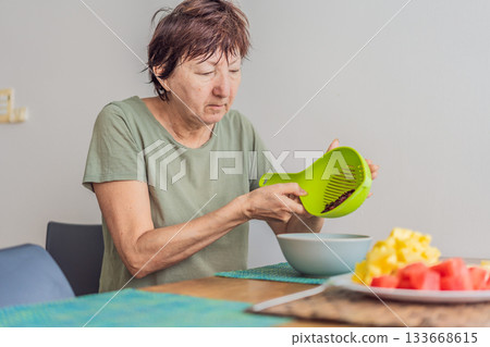 Unaltered senior woman enjoying a calm breakfast at the dining table in a bright home setting. Concept of healthy lifestyle, mindful eating, peaceful morning routine, comfort, wellbeing and everyday 133668615