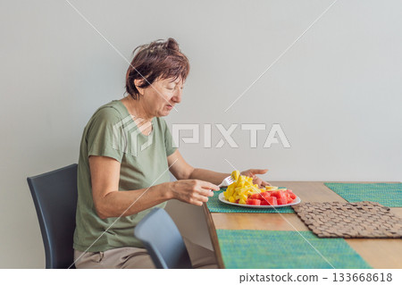 Unaltered senior woman enjoying a calm breakfast at the dining table in a bright home setting. Concept of healthy lifestyle, mindful eating, peaceful morning routine, comfort, wellbeing and everyday Unaltered senior woman enjoying a calm breakfast at the dining table in a bright home setting. Concept of healthy lifestyle, mindful eating, peaceful morning routine, comfort, wellbeing and everyday 133668618