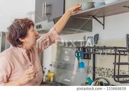 Elderly woman cooking in the kitchen, preparing a homemade meal with care and joy. Concept of healthy aging, independence, domestic life, culinary routine, and active senior lifestyle at home 133668639