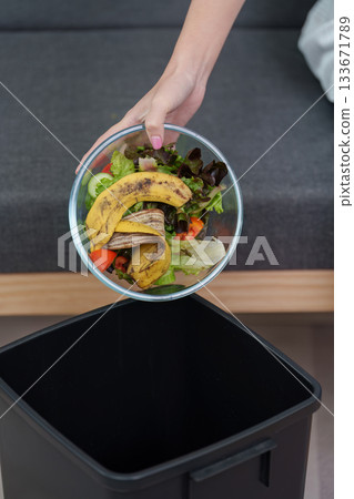 Sustainable living. Woman discarding food waste into trash bin. 133671789