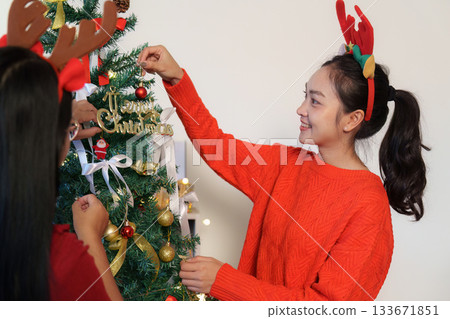 Joyful Christmas Tree Decorating. Young woman smiling while adding ornaments. 133671851