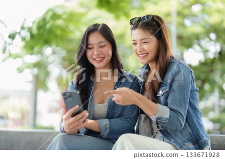 Friendship and Connection. Two young women enjoying a moment together while using a smartphone outdoors. 133671928