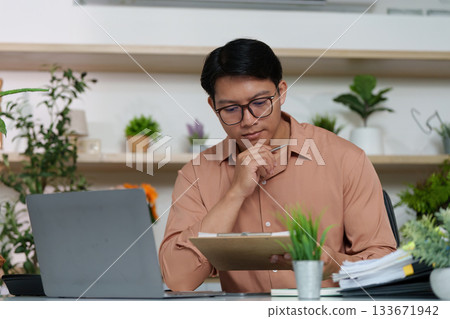 Thoughtful Professional. Man reviewing notes in modern workspace. Thoughtful Professional. Man reviewing notes in modern workspace. 133671942