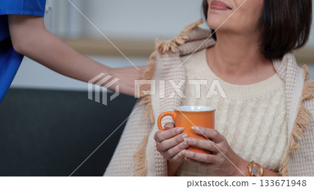 Caregiver providing comfort with warm drink to elderly woman 133671948