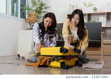 Travel Planning: Friends struggling to close their packed suitcase Travel Planning: Friends struggling to close their packed suitcase 133671965