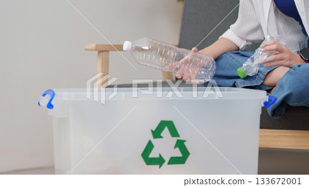 Recycling. Individual sorting plastic bottles into recycling bin at home. 133672001