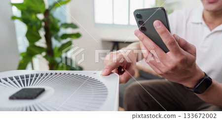 Smart Technology. User controlling air purifier with smartphone in modern home. Smart Technology. User controlling air purifier with smartphone in modern home. 133672002
