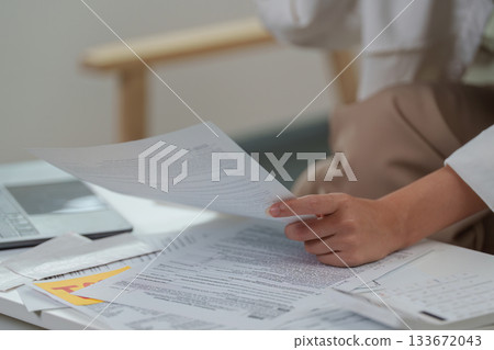 Paperwork Chaos. Close-up of woman holding tax documents while sitting at a desk. 133672043