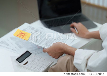 Tax Preparation. Individual reviewing tax documents with calculator and laptop. 133672044
