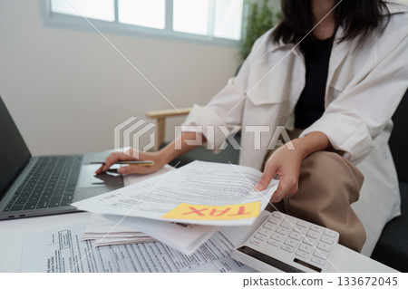 Tax Management. Individual sorting tax papers with calculator and laptop. 133672045